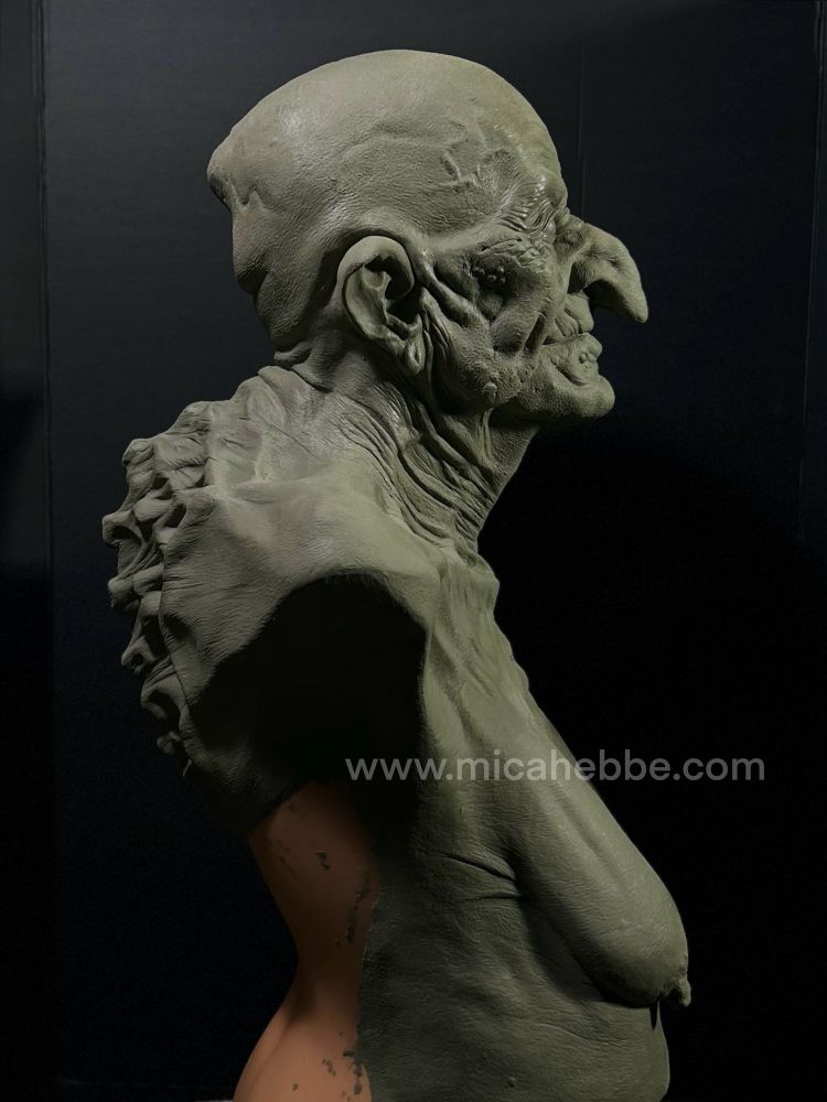 Clay sculpture of a witch from the waist up for a latex mask. She is naked and her skin is stretched over her bones. She has a slight smile. Side view