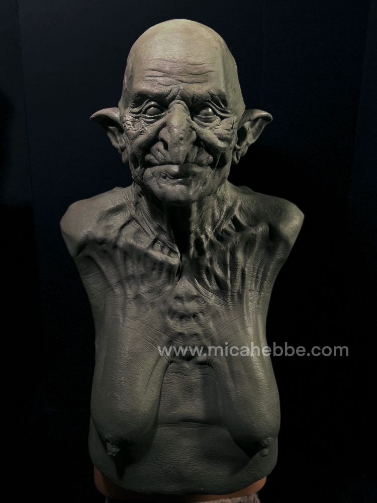 Clay sculpture of a witch from the waist up for a latex mask. She is naked and her skin is stretched over her bones. She has a slight smile. Front view. 