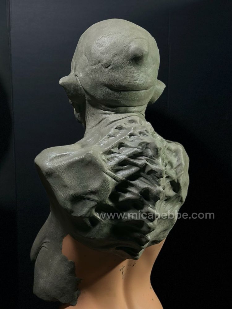 Clay sculpture of a witch from the waist up for a latex mask. She is naked and her skin is stretched over her bones. She has a slight smile. 3/4 back view