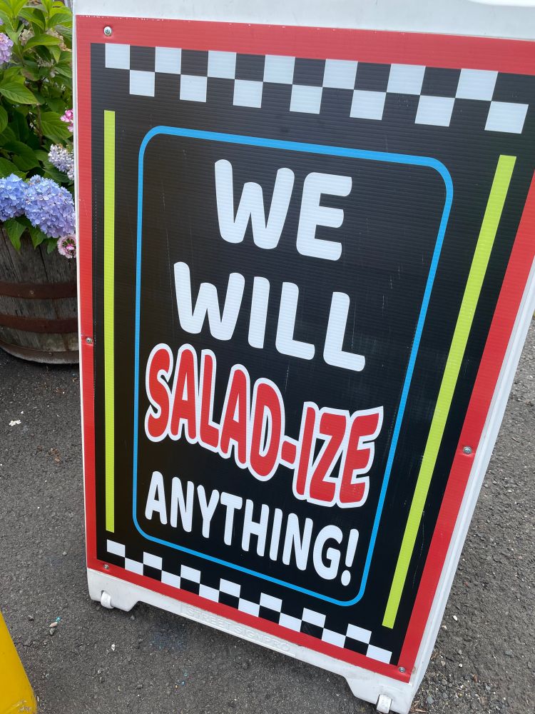 A sandwich board reading “We will salad-ize anything!”