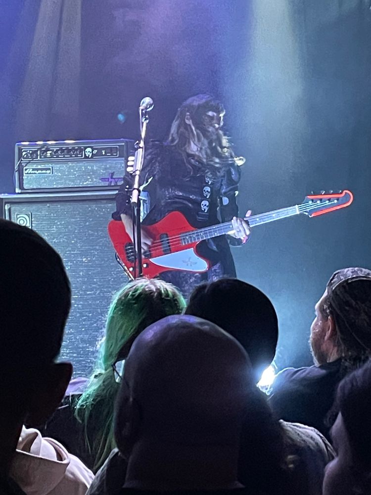 Nikki, the bassist for Silversun Pickups, is between amps and a mic while she plays a red bass and her hair is swaying with the beat