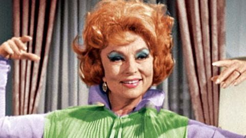 Still of Endora from Beweitched — an older woman with bright red hair and blue eye shadow, wearing  green vest over a purple colored shirt