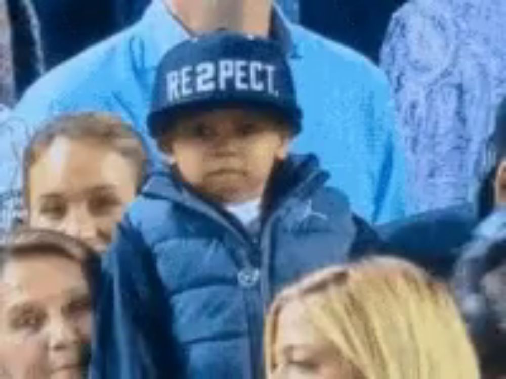 a child wearing a hat that says respect is sitting in a crowd of people