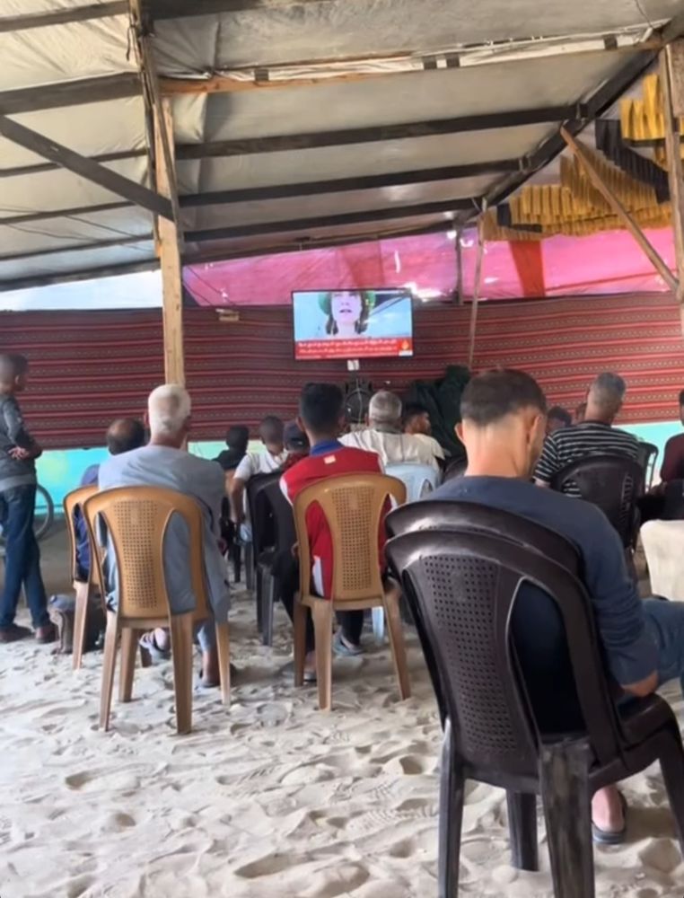 Some Gazans are watching TV under a tent, where Greta Thunberg is speaking.

