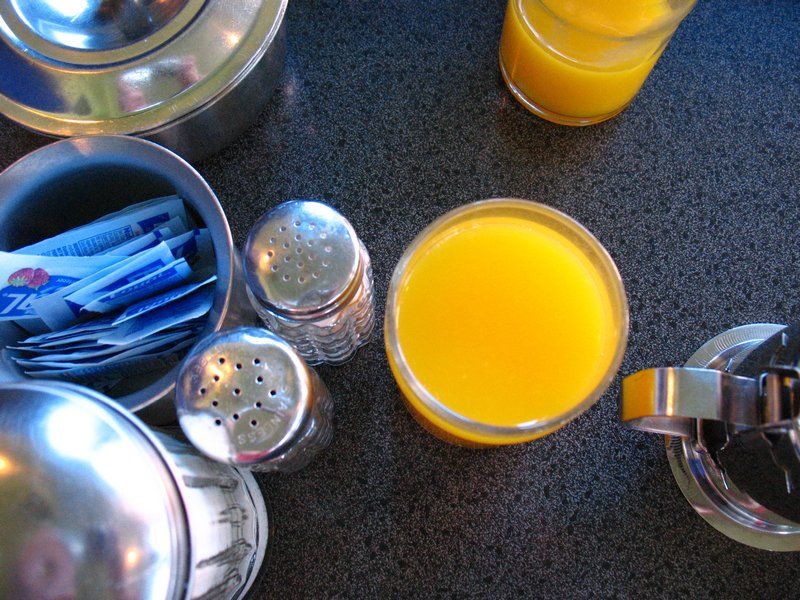 A diner table seen from above with metal containers for salt, pepper, sugar, teawater and milk, plus sugar packets and orange juice in glasses.  Photo by CC Lena Struwe