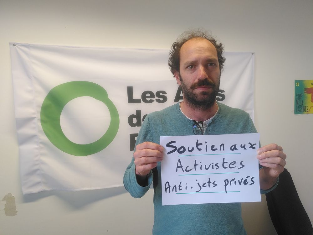 Frédéric Amiel, coordinateur des Amis de la Terre, tient une pancarte "soutien aux activistes anti-jets privés" devant un drapeau des Amis de la terre.
