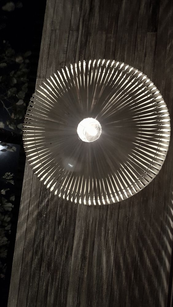 Eine balinesische Deckenlampe in einem Pavillion. Das Licht fällt durch feine Lücken  eines sternförmig angeordneten Bastschirmes.