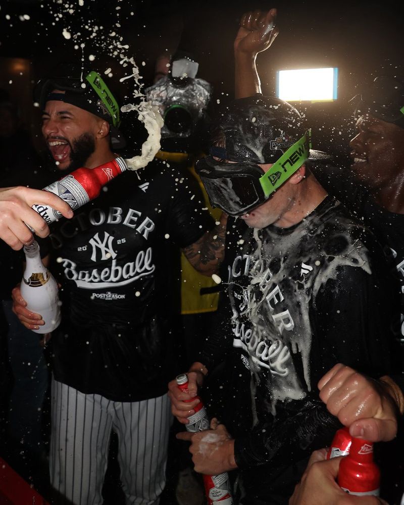 Yankees players celebrate with Budweiser in the clubhouse after clinching a spot in the ALDS on Thursday night. They are wearing dark blue "October Baseball" t-shirts with the Yankees logo on the front.