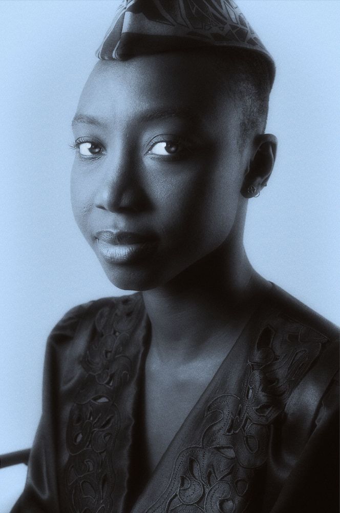 portrait of a young senegalese woman in lustrous and embroidered silk dress and ribbed cap of african design