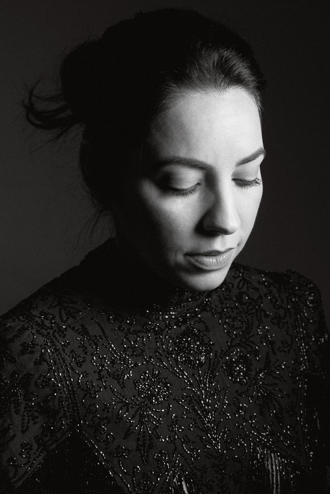 portrait of a young Nicaraguan female in a black sequined blouse, with her hair up in a bun behind her head and her eyes looking down at the floor
