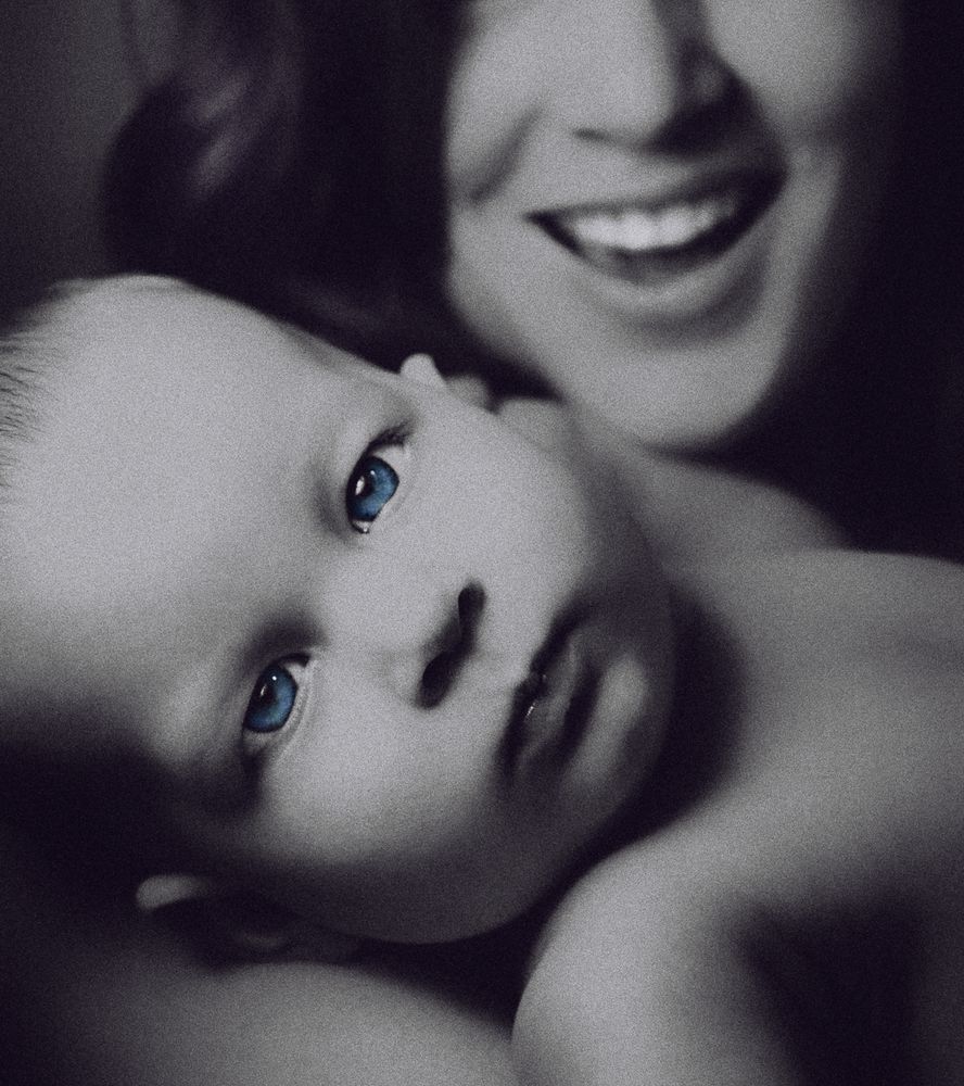portrait of baby Eden looking serenely into the camera while her mother coos her on in the distance