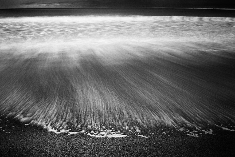 a long exposure of white-wash from the sea swoops up onto the sand and then slowly ebbs away - leaving a line of suds and long trails behind 