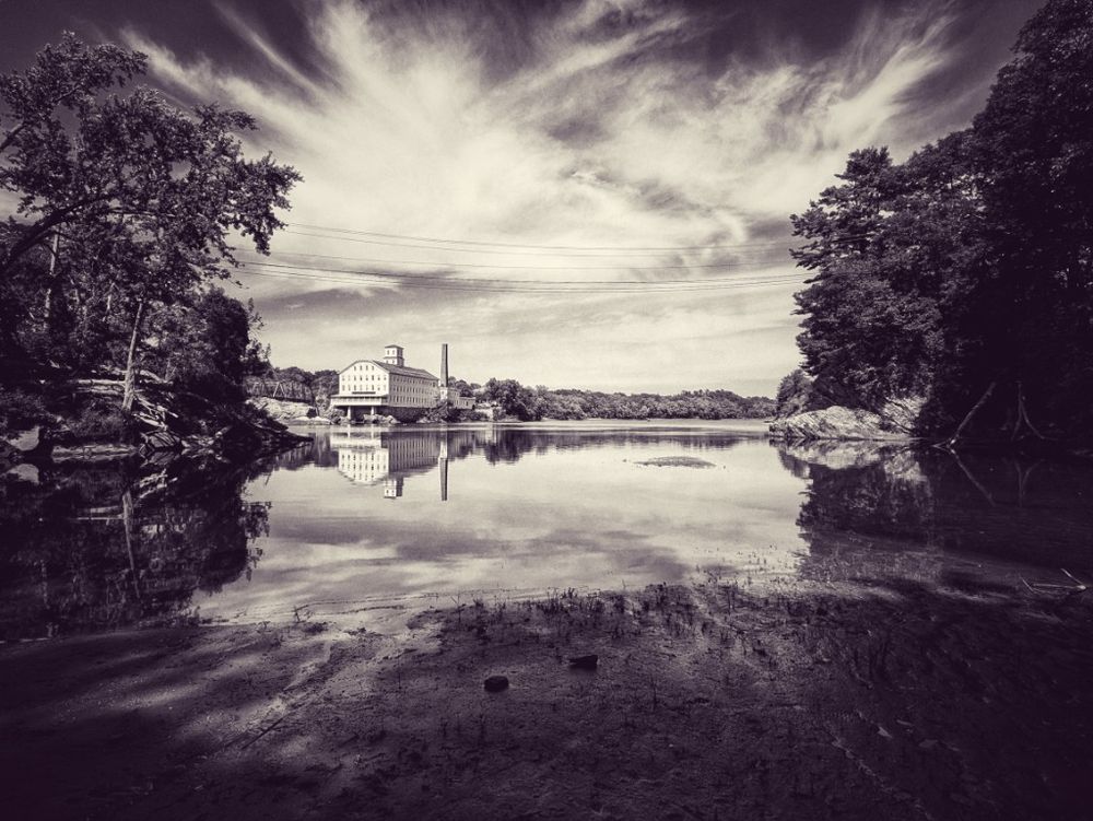 an expansive blue sky with fluffy white clouds adorns a still and timeless river bank inlet at low tide... hewed in by forest, rock and soft mudflats