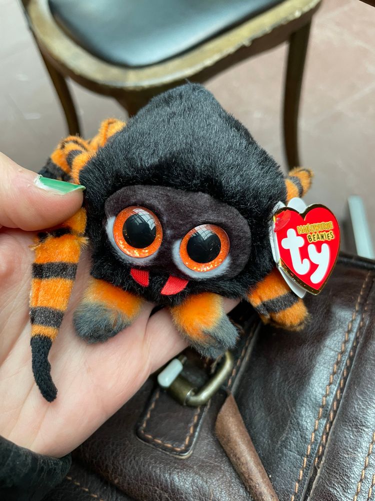 En hand som håller i en gosedjursspindel som är ungefär lika stor som handen 