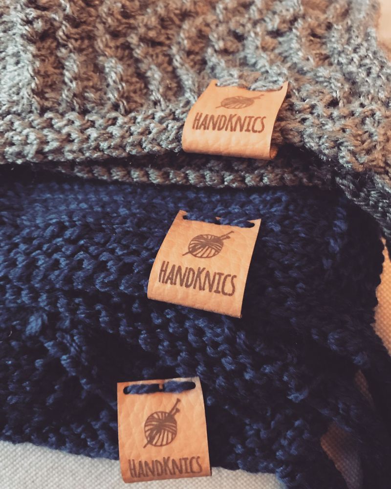 Pile of hand knitted items with beige labels showing a ball of yarn and the name HandKnics