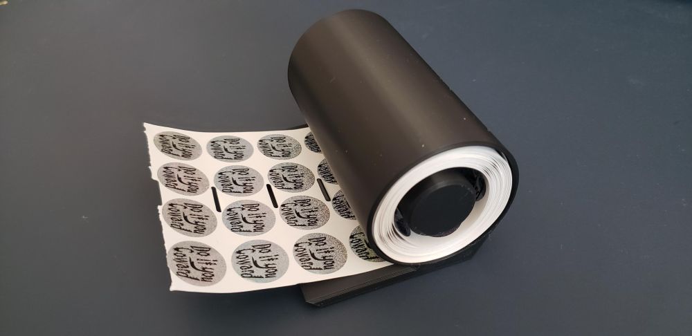 A side view of the sticker spool holder showing a very full reel of the "Do it you Coward" stickers waiting to be dispensed.