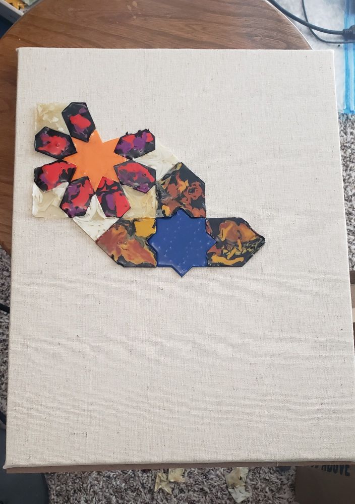 A stretched canvas with some of the homemade melted plastic zellij tiles nestled in place, starting at the center and progressing to the top left.