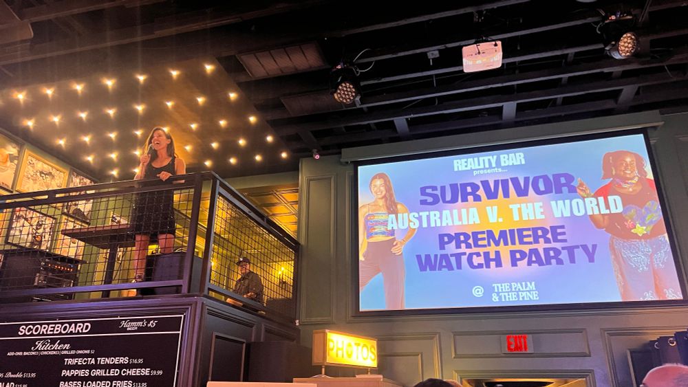 parvati is standing on a balcony with a mic introducing survivor au vs the world premiere to all the fans at the bar
