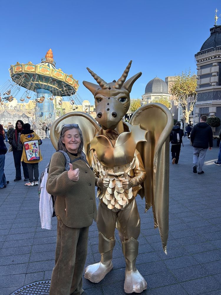 My mom standing besides one of Phantasialand's dragon mascots, with a wave swinger in the background, in the Berlin area of the park.