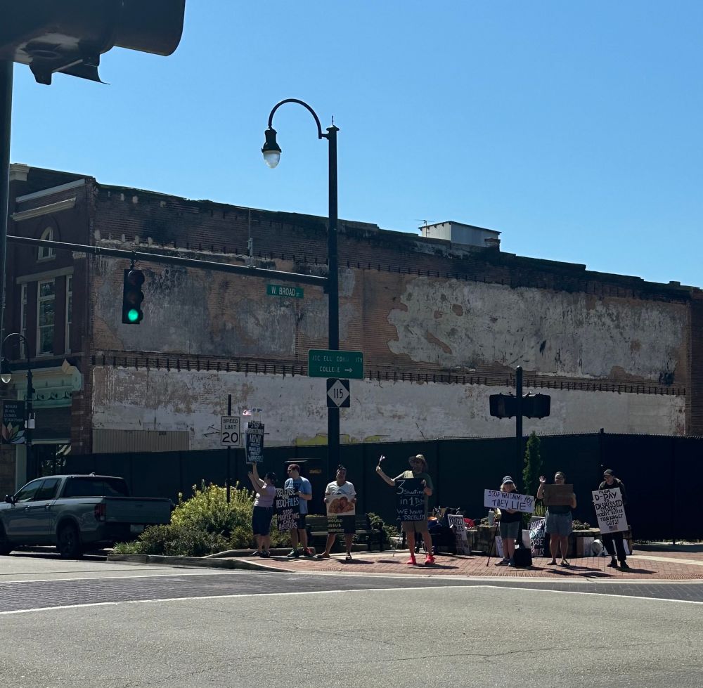 protestors on a street corner in statesville north carolina with signs calling for the impeachment of trump and decrying the lies of fox news 