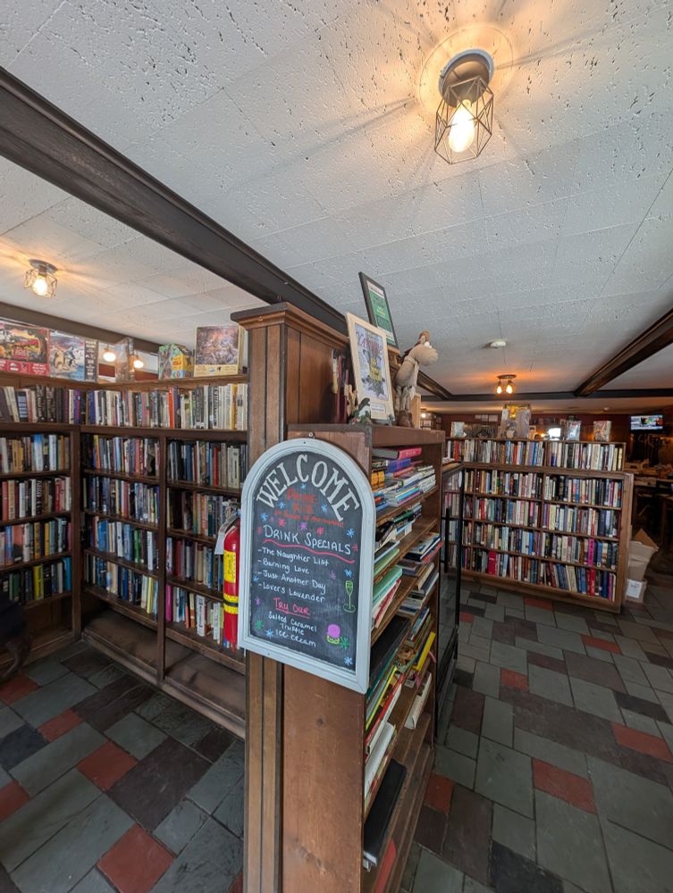 A large room with shelves lined with books and a sign that reads Welcome above a drink menu