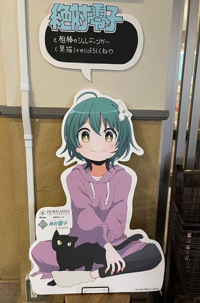 A cutout of cute anime girl with short green hair with a purple hoody and grey slacks with a black cat introducing themselves as Zettai Reiko and Schrödinger, possible mascots of the physics department at Hokudai. 