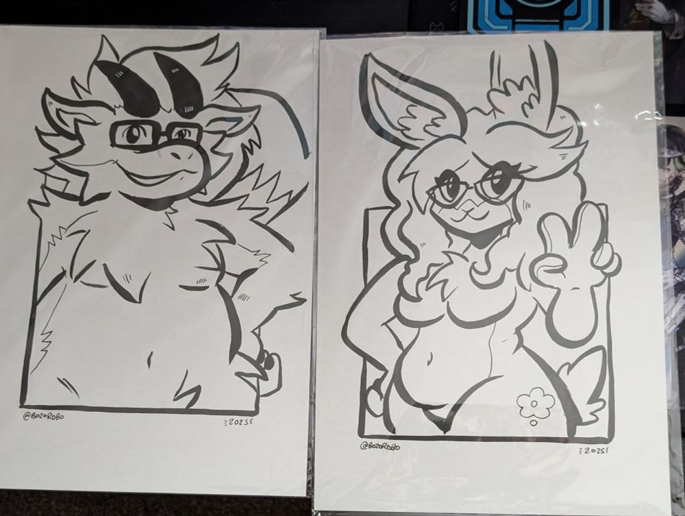 Two A4 sheets of paper on a desk, the one on the left has an inked sketch of my furred dragon fursona Raggak, and the right has an inked sketch of my wife's bunny fursona Shauni. Both pieces were drawn by bozorobo!