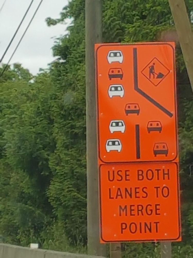Orange road sign demonstrating a zipper merge