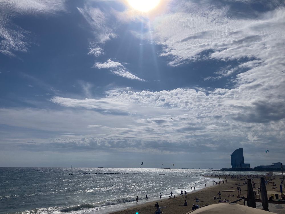 Sun shining on the wild vision of Barcelona beach, huge waves crashing onto the shore with the outline of big 90s scyscrapers on the horizon 