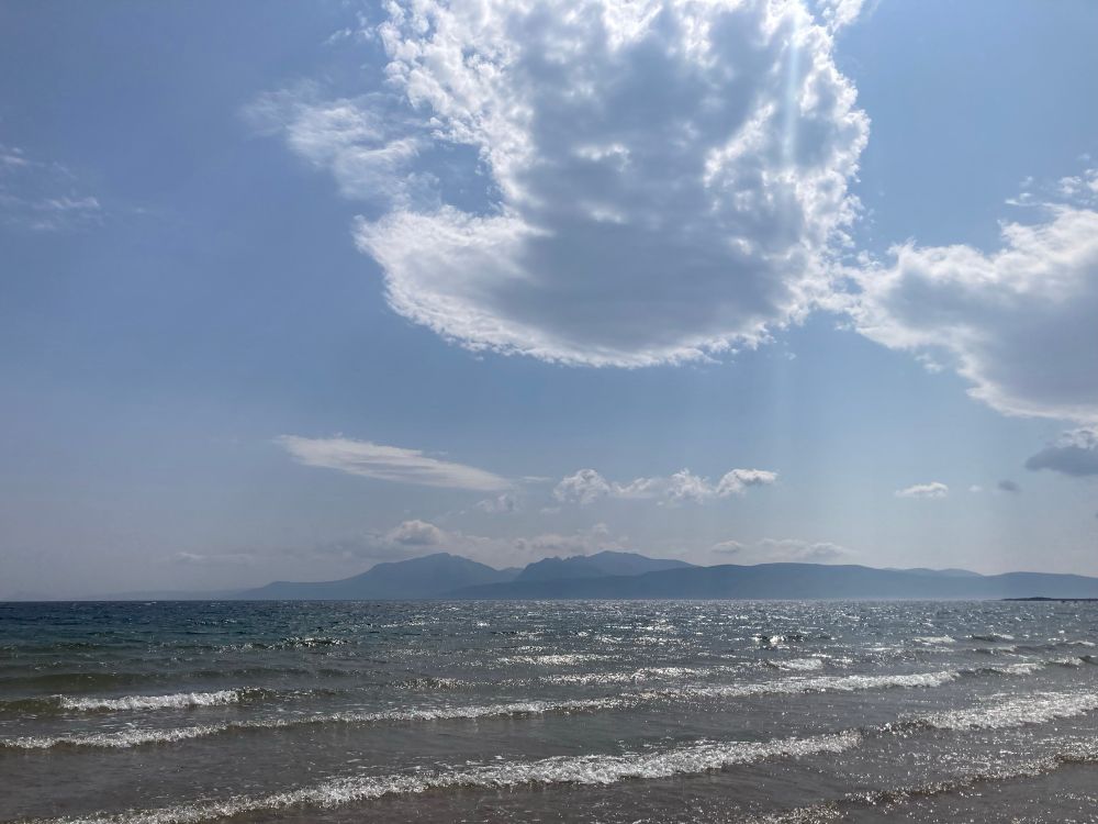 Sunshine sparkling on the waves at Scalpsie Bay, with the jagged Arran peaks across the sea in the background 