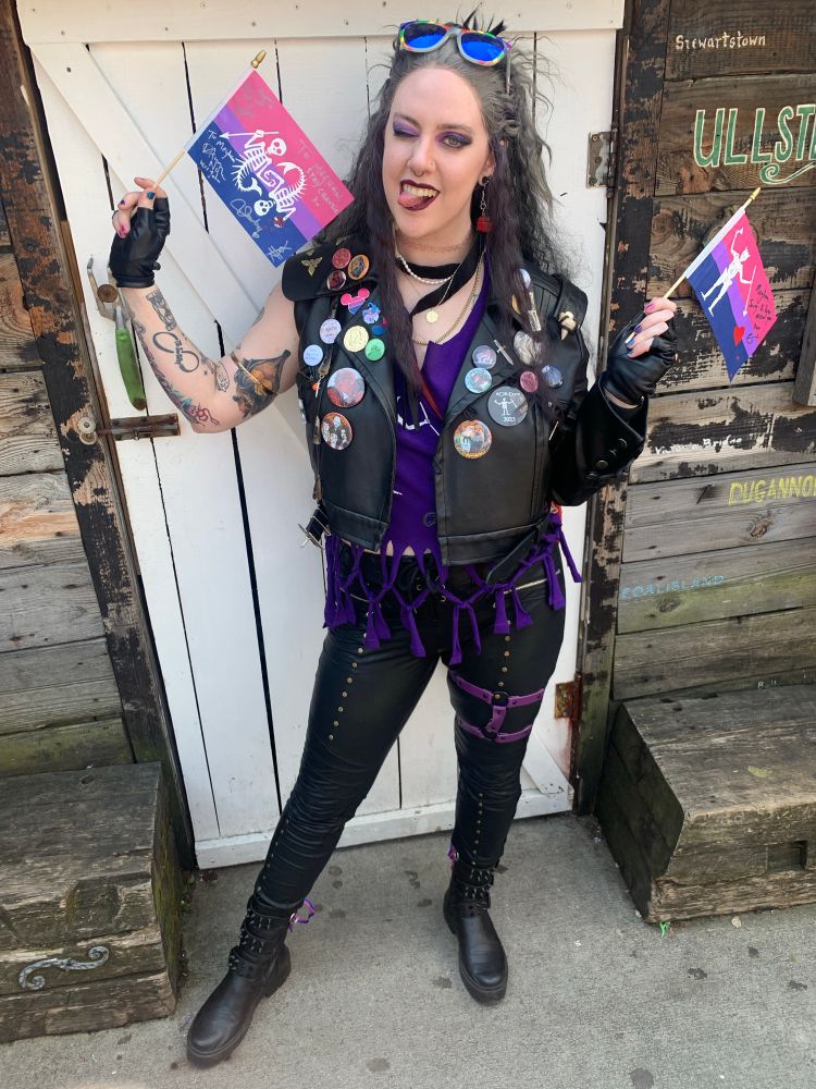 Lizzy in a modern/canon mash up Ed Teach cosplay holding up 2 small bisexual OFMD flags