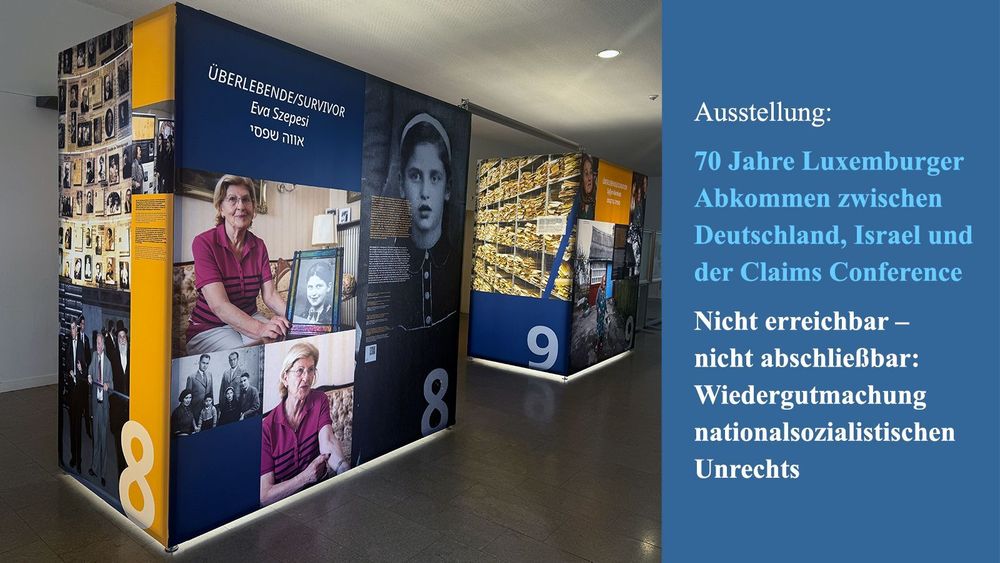 Foto der Wanderausstellung mit großen, farbigen Würfeln im Foyer des IG-Farben Hauses.

Im Vordergrund ist ein Ausstellungsmodul mit der Nummer 8 zu sehen, das Eva Szepesi, eine Holocaust-Überlebende, porträtiert. Zu sehen sind Fotos von ihr als Kind und im Alter, sowie historische und persönliche Bilder mit Familienmitgliedern und anderen Zeitzeugen.

Daneben ein weiteres Modul mit der Nummer 9, das Dokumentenberge und Archivbilder zeigt.

Rechte Bildhälfte (Text auf blauem Hintergrund):
Ausstellung:
70 Jahre Luxemburger Abkommen zwischen Deutschland, Israel und der Claims Conference

Nicht erreichbar – nicht abschließbar:
Wiedergutmachung nationalsozialistischen Unrechts