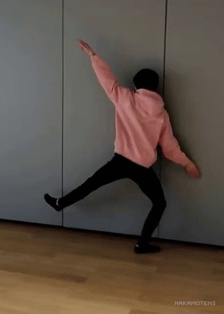 a person in a pink hoodie and black pants is dancing in front of a wall .