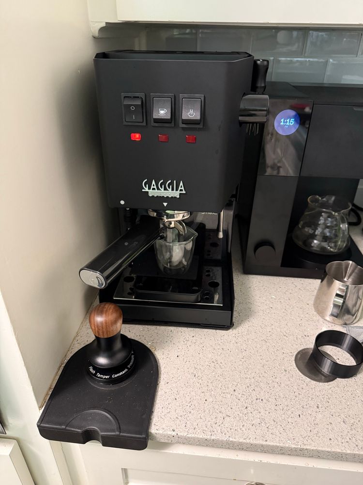 A Gaggia Classic Evo Pro espresso machine in thunder black with a tamper and tamping mat in the foreground.