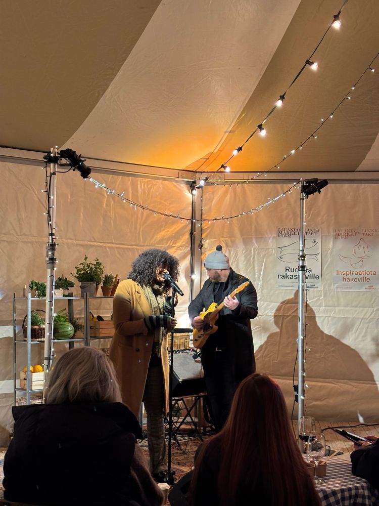 Soul-laulaja Emilia Sisco ja kitaristi esiintymässä tunnelmallisesti valaistussa teltassa Helsingin Vanhan Kauppahallin kupeessa.