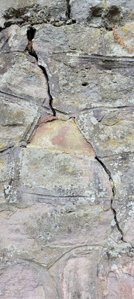 Steinwand mit Rissen, man könnte eine Brust erkennen, und ein Gesicht davor, der Mund an der Brustwarze