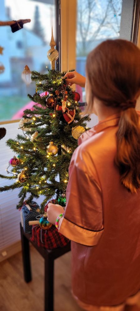 Mädchen schmückt den 20 Jahre alten Weihnachtsbaum, unter dem Baum liegen Geschenke