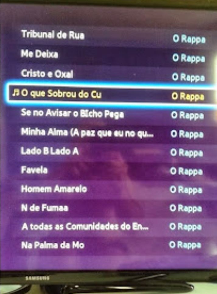 Foto de TV Samsung que não reconhece os acentos gráficos PT-BR. Tela mostra sucessos do Rappa como Na Palma da Mo, Cristo e Oxal e O que Sobrou do Cu