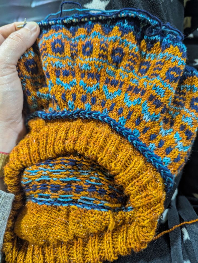 A piece of hand knitting in progress - stranded colour work jumper in orange and blues 