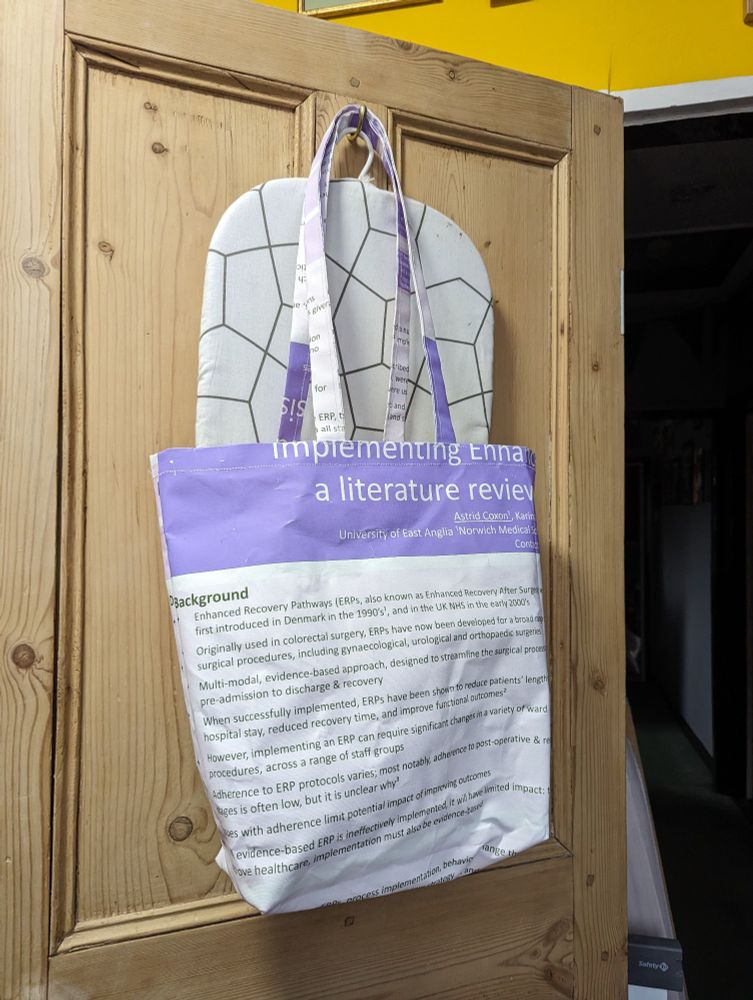 A tote bag made from a fabric conference poster. The title of the poster suggests the poster was of a literature review of implementing.... Something.