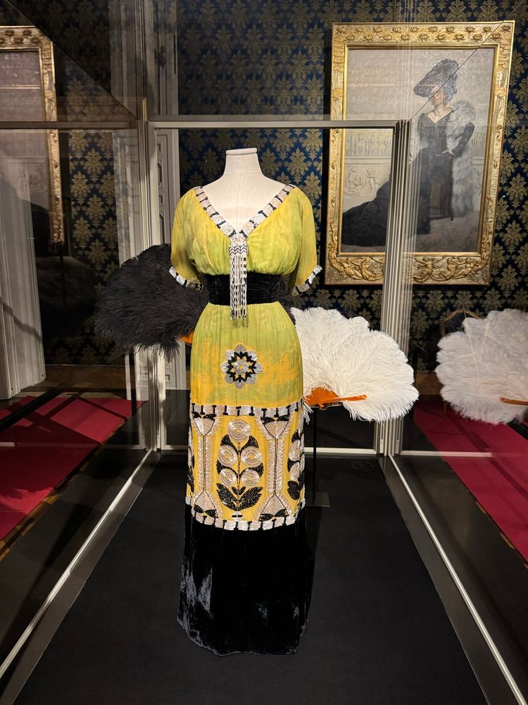 Woman's dress
C. 1913
Label:"A La Ville de Lyon / Raphael Goudstikker Naples"
MMC, inv. TA 6846
Silk chiffon dress dyed in shades of green and yellow. The deep V-neckline is edged with a jewel decoration made of black and white glass bugle beads and small pearl beads running down from the breast to the waist The short sleeves are adorned at the hem with the same pearl and bugle bead motif. The waistline is underscored by a wide black silk velvet band. The lightly flaring skirt, which is longer at the back to form the hint of a train, is elegantly decorated with a geometrical decoration of large stylised plants clearly inspired by the Jugendstil.
This dress belonged to the Countess Margaret Brinton White Sa-vorgnan di Brazzà.
Donated by the Associazione Amici della Galleria del Costume, 1999