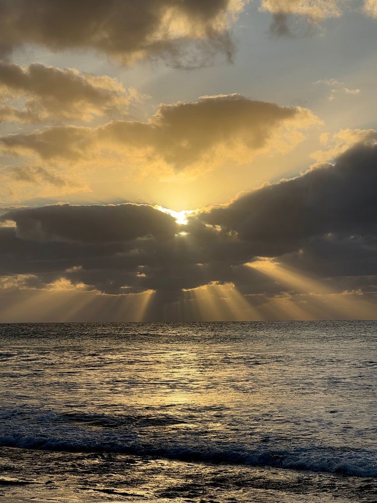 Sun behind clouds with many rays of sunshine reaching down to sea