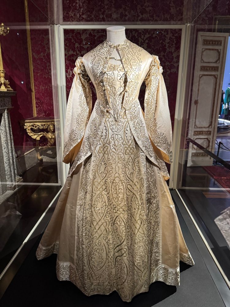 Wedding gown
1862
MMC, inv. TA 6790
This magnificent three-piece ivory silk satin ceremonial gown comprising a bodice, a jacket and a skirt, was made in 1860. Its shape, with a wide lightly gathered dome-shaped skirt that is longer at the back and sleeves flaring en pagode attached at the shoulder by gathering en coulisse, is reminiscent of a Renaissance gown, reflecting the 19th century interest in revivals.
The extremely fine embroidery, involving the application of gilded metal yarn spikelets in a complex knotted weave composition is also inspired by the Renaissance.
Donated by Pia Teresa Mallaby Carmi, 1997