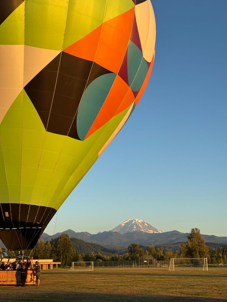 View of colorful hot air balloon landed in a soccer field with Mt Rainier/Tahoma in distance. 
