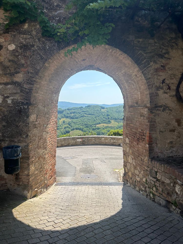 A stone archway looking out over green Tuscan hills. 