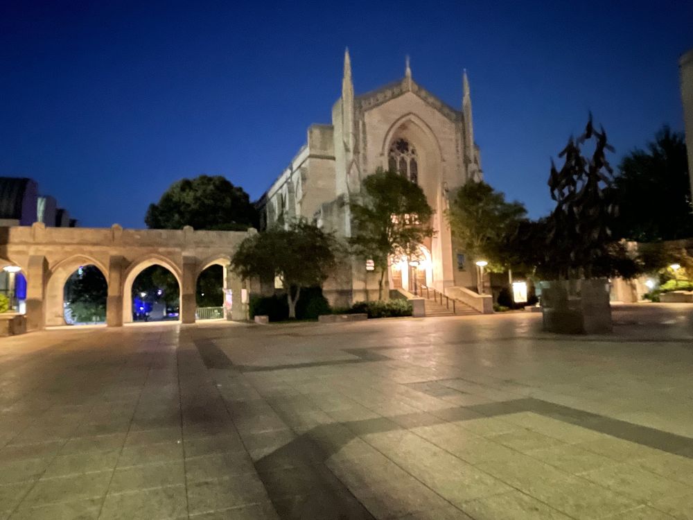 Boston University's Marsh Plaza with sandy colored stone buildings, chapel, & archways illuminated at Twilight