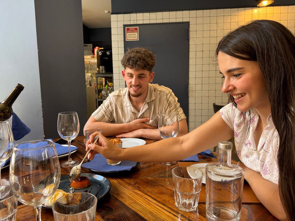 A young couple smiling in a restaurant, where the woman is dividing the desserts for everyone to sample. 