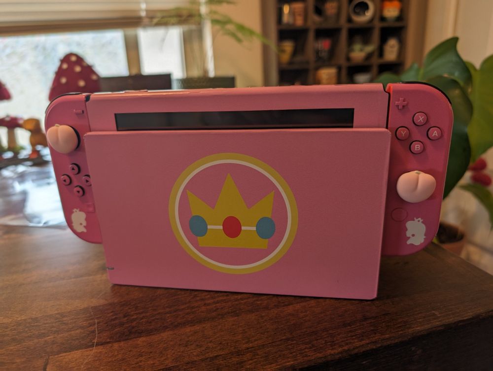 Front of my Nintendo Switch in its dock with the Lux Brand Minimalist Princess Peach Skin and Peach joystick caps