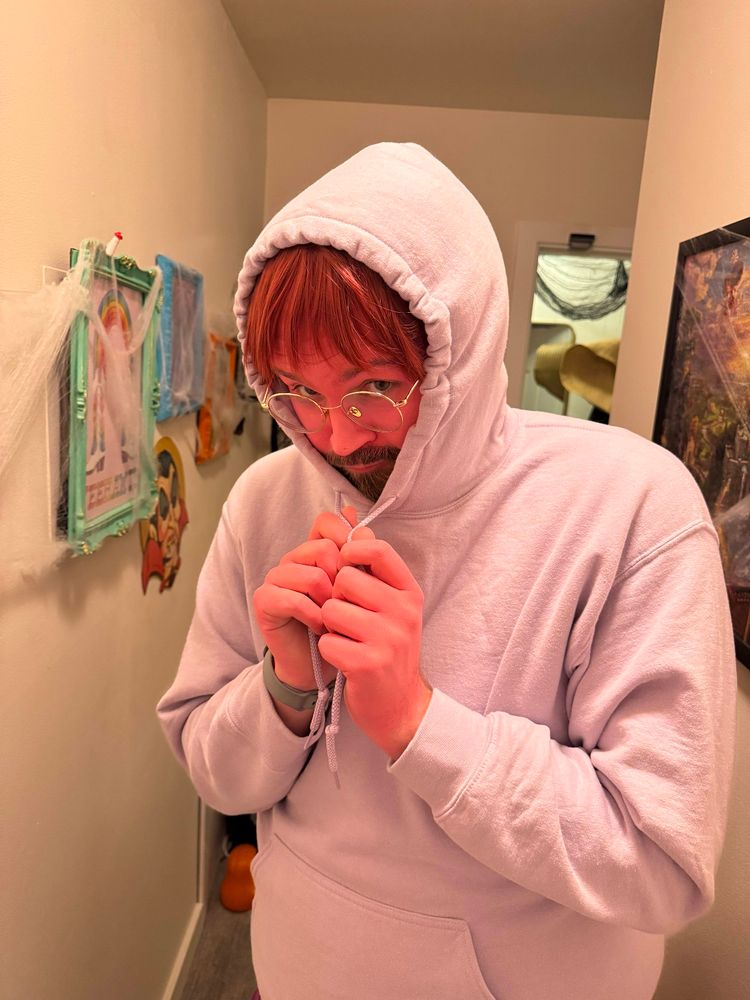 Me in a purple hoodie, maroon wig, and pink body paint doing the Embarrassment pose from Inside Out 2