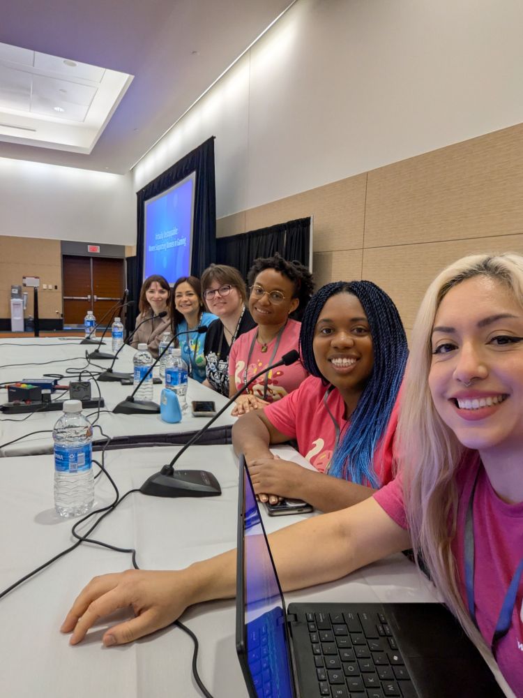 Women smiling at a long table at a conference 